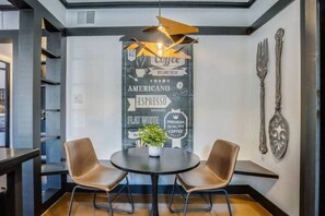 Un café moderne avec deux fauteuils en cuir, une table centrale agrémentée d’une plante, et un mur décoré de motifs et d’ustensiles liés au café.