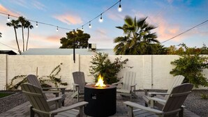 An outdoor patio with a circular fire pit surrounded by Adirondack chairs, a white wall, and string lights. - The Minnezona Modern-Old Town (Scottsdale)