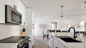 A modern kitchen with white cabinetry, a large island with a sink, and a dining area with black chairs and a table. - The Minnezona Modern-Old Town (Scottsdale)