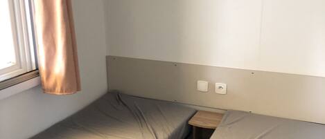 A small, single-bed room with a window, a wooden nightstand, and a shelf above the bed.
