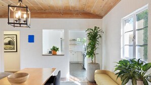 A cozy living room with a wooden dining table, a sofa, and a large window. - Dog-Friendly Bungalow with Private Pool (Palm Springs)