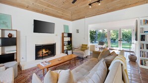 A spacious living room with a fireplace, a large sofa, a coffee table, and a bookshelf. - Dog-Friendly Bungalow with Private Pool (Palm Springs)