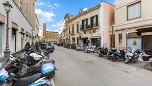 A street lined with parked scooters and cars, buildings with commercial establishments, and a clear sky. - 3141 B&b Incentro Comfort Suite - Central Suite by Barbarhouse (Lecce)
