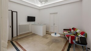 Un soggiorno moderno con un divano bianco, un tavolino, una TV a parete e un lampadario.