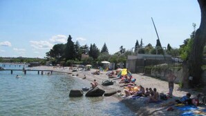 Una playa con aguas cristalinas, gente tomando el sol y un muelle al fondo.