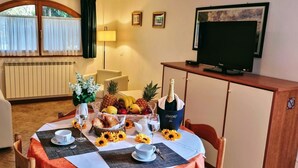 Un comedor con una mesa dispuesta para dos personas, con una cesta de frutas, vino y una botella de champán.
