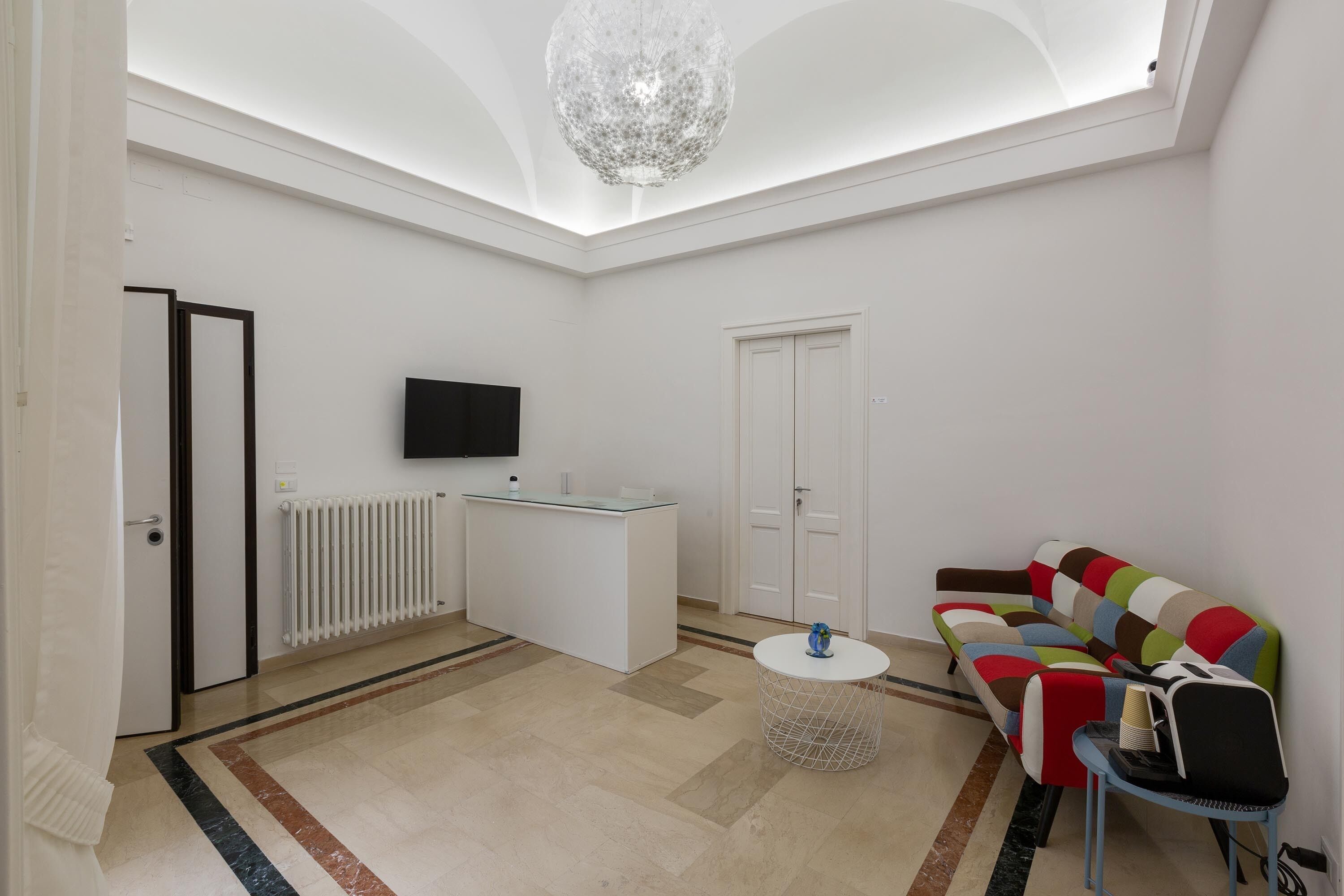 A modern living room with a white sofa, a coffee table, a TV mounted on the wall, and a chandelier.
