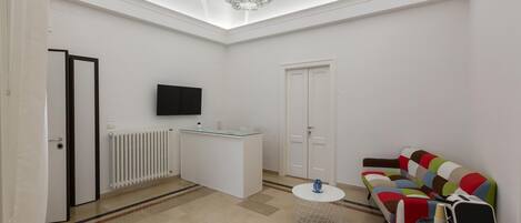 A modern living room with a white sofa, a coffee table, a TV mounted on the wall, and a chandelier.