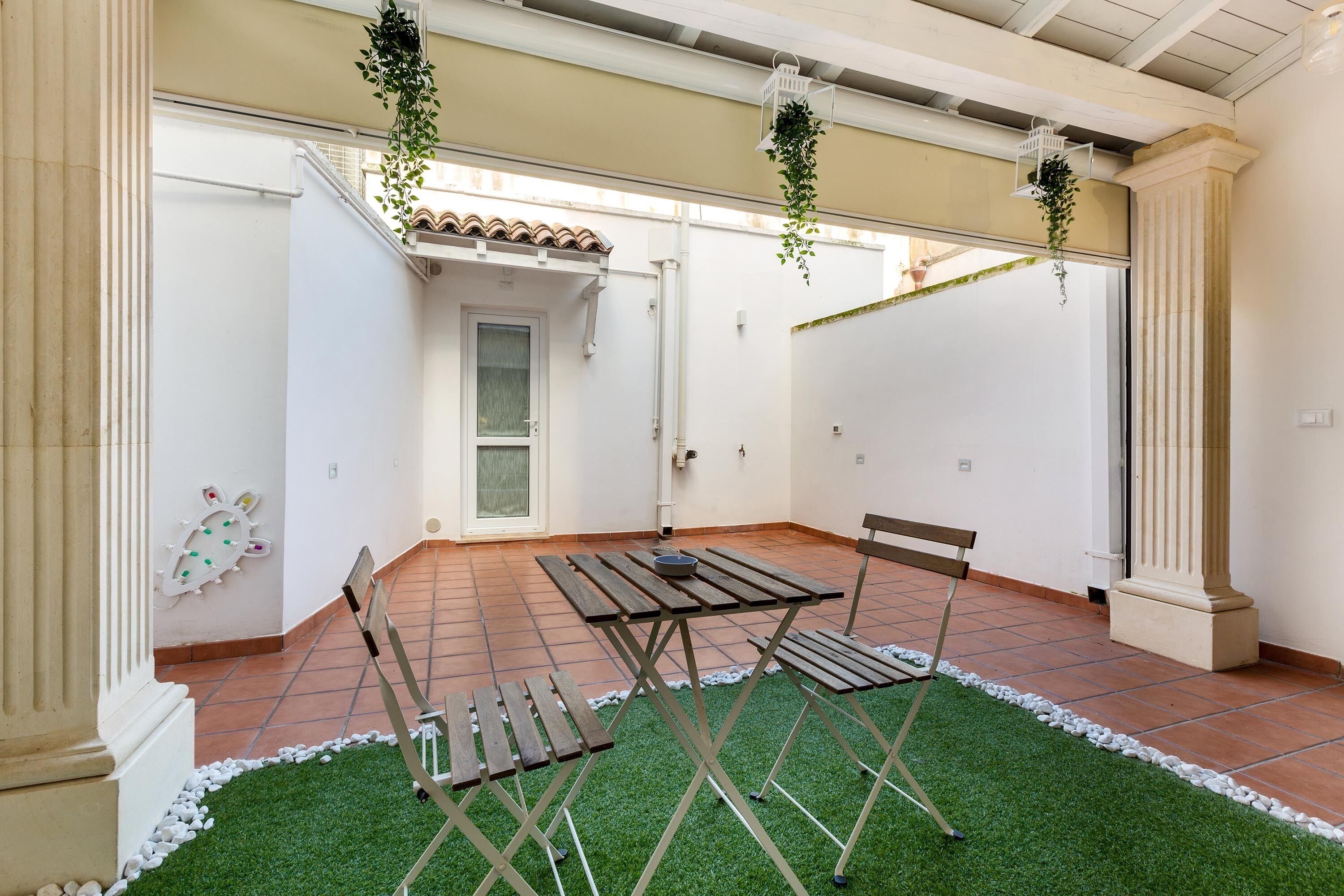 A patio with a table and chairs, surrounded by white walls and a tiled floor.
