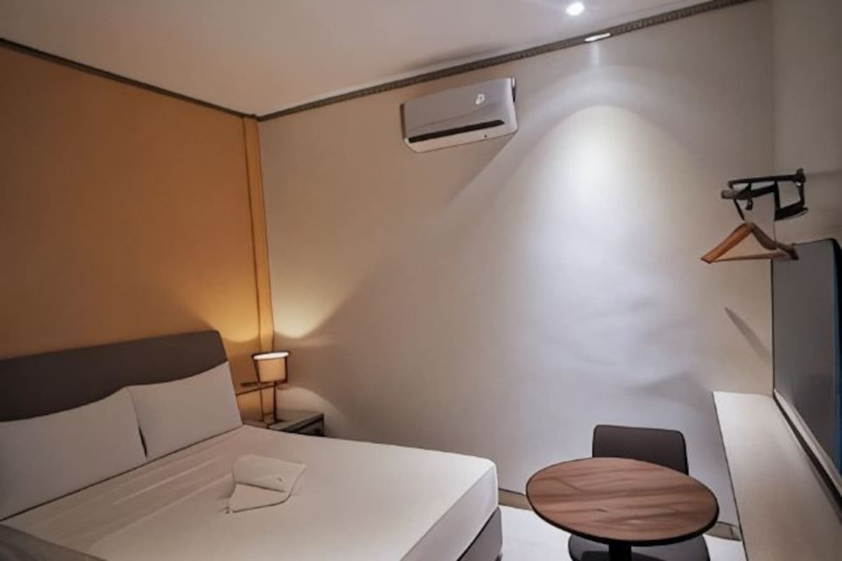 A hotel room with a bed, bedside table, lamp, and a small round table.