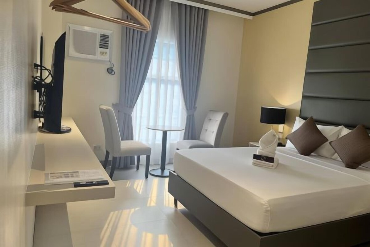 A modern hotel room with a bed, bedside table, chair, and a small round table.