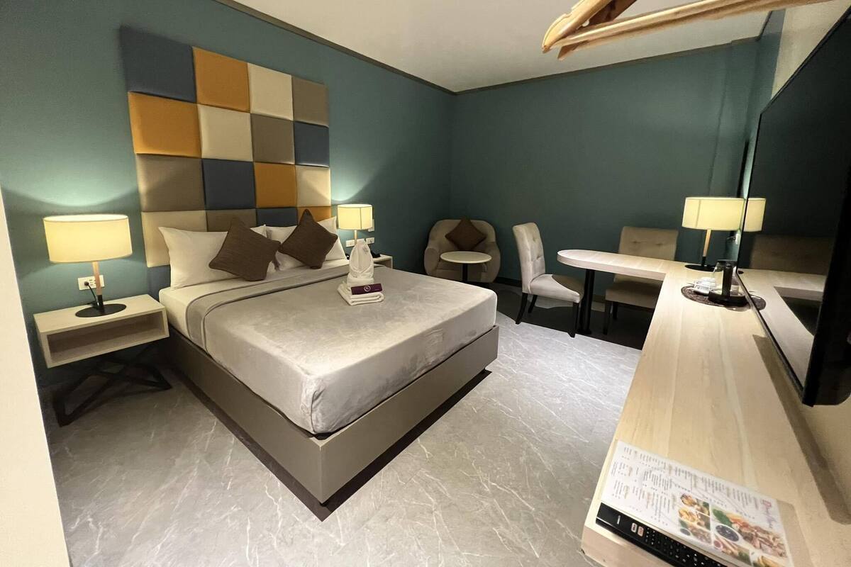 Habitación de hotel con cama, dos mesitas de noche con lámparas, una pequeña mesa redonda con una silla y un espejo grande.
