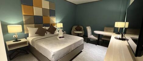 A hotel room with a bed, two bedside tables with lamps, a small round table with a chair, and a large mirror.