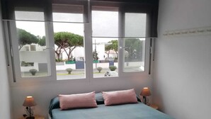 A bedroom with a bed, two bedside lamps, and a window with a view of the outside. - Modern beachfront apartment San Miguel (El Rompido)