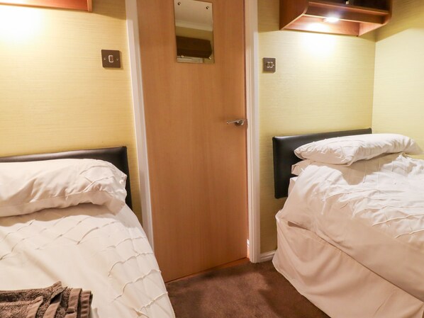 A hotel room with two single beds, a wooden door, and a small mirror on the wall. - Washburn Lodge (Harrogate)