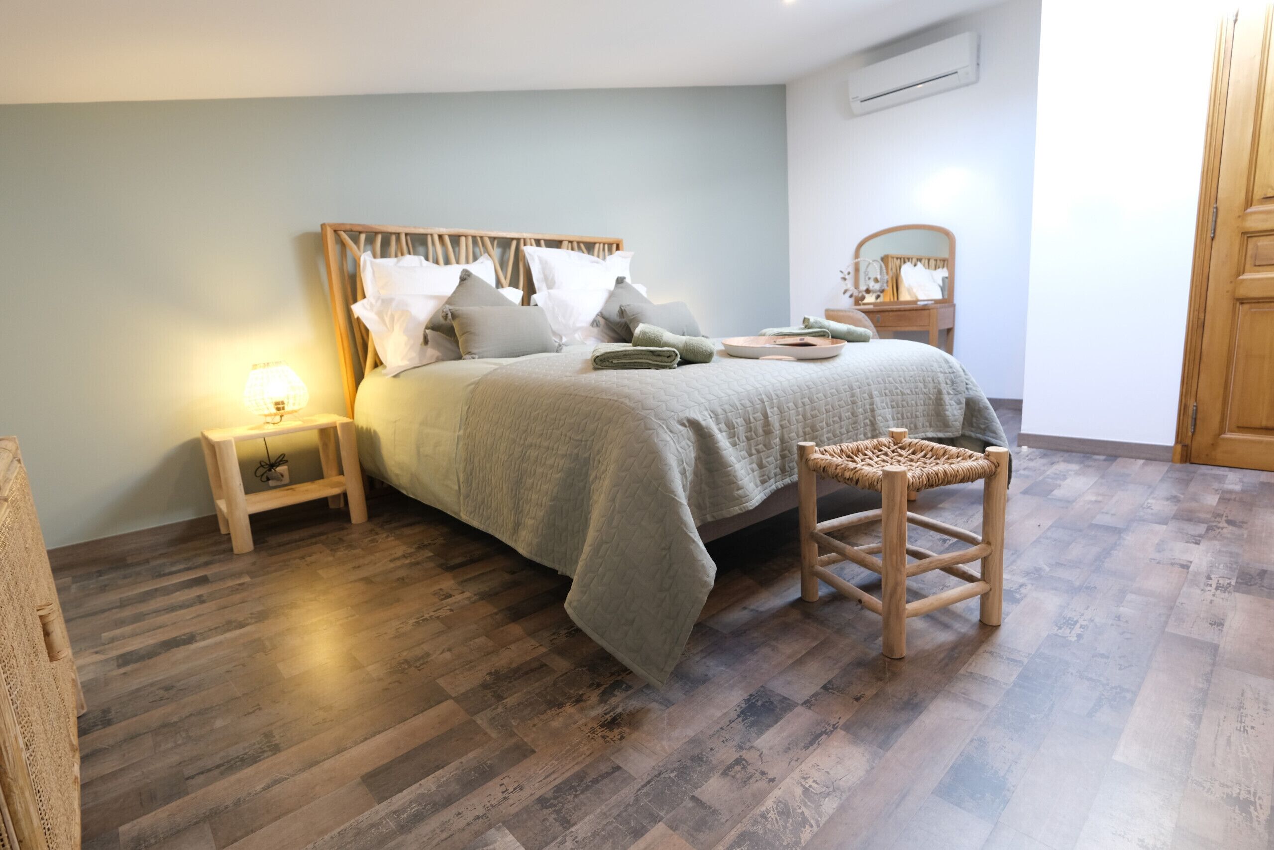 Un dormitorio con cama, mesitas de noche, una silla de madera y un espejo.