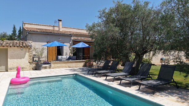Une piscine avec des chaises longues et des parasols, une porte en bois et un mur en pierre.