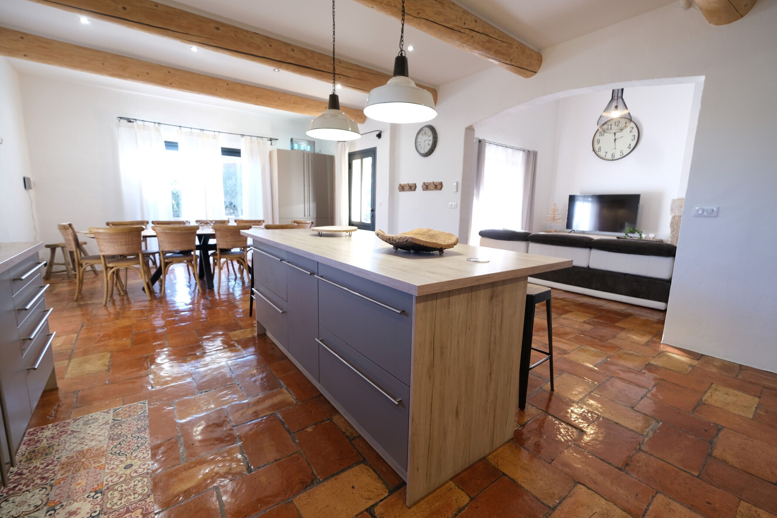 A spacious kitchen with a large island, wooden beams, and a tiled floor.