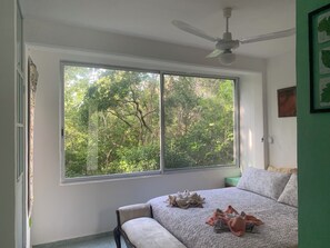 A bedroom with a large window, a ceiling fan, and a bed with pillows and blankets. - Remarkable Studio in Jungle of Chemuyil, Tulum (Tulum)