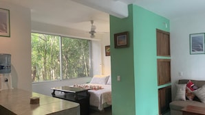 Una stanza con un letto, una scrivania, un dispenser d'acqua, una finestra vista alberi e una ventola a soffitto.