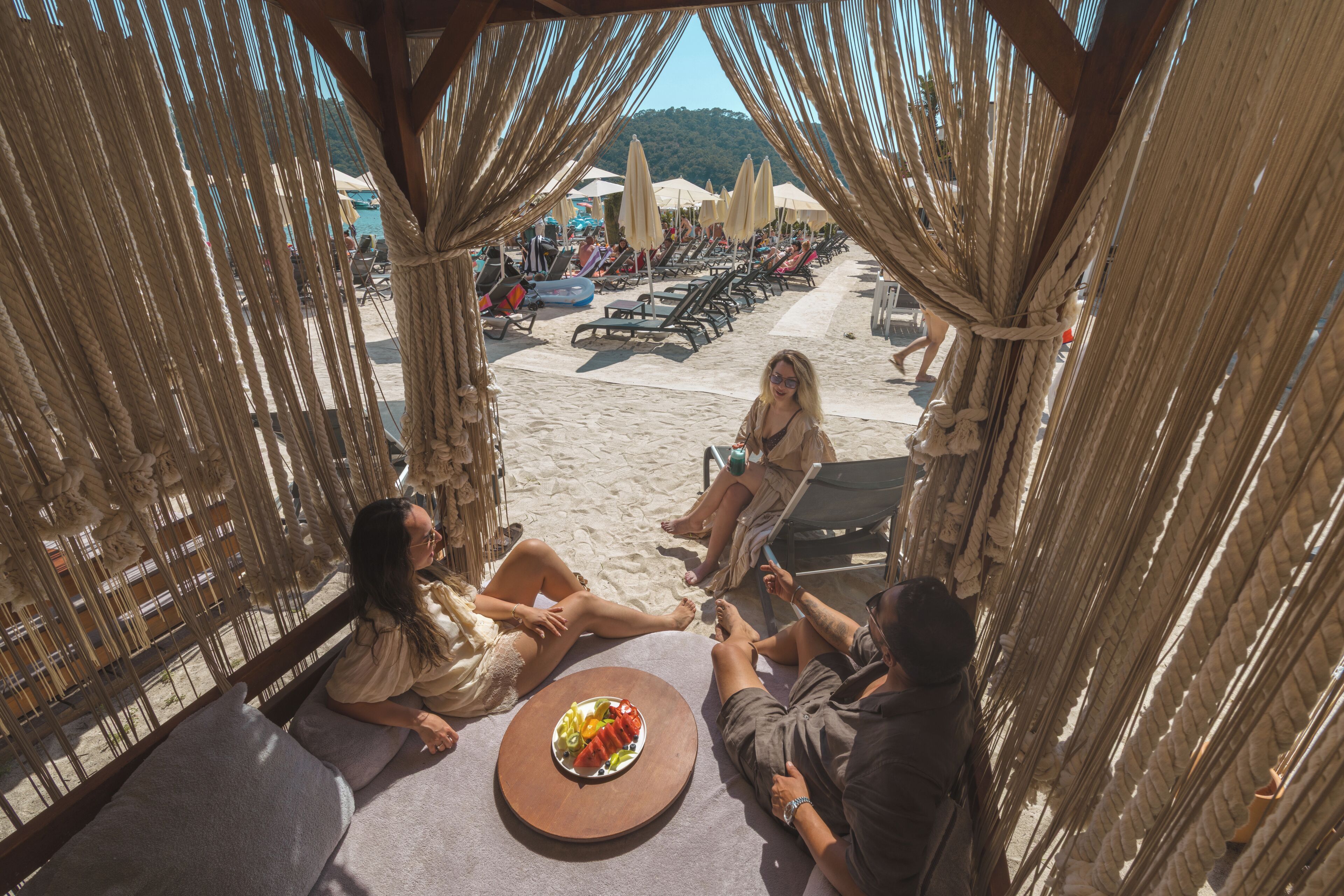 Un área de descanso junto a la playa con mesa, sillas y sombrillas.