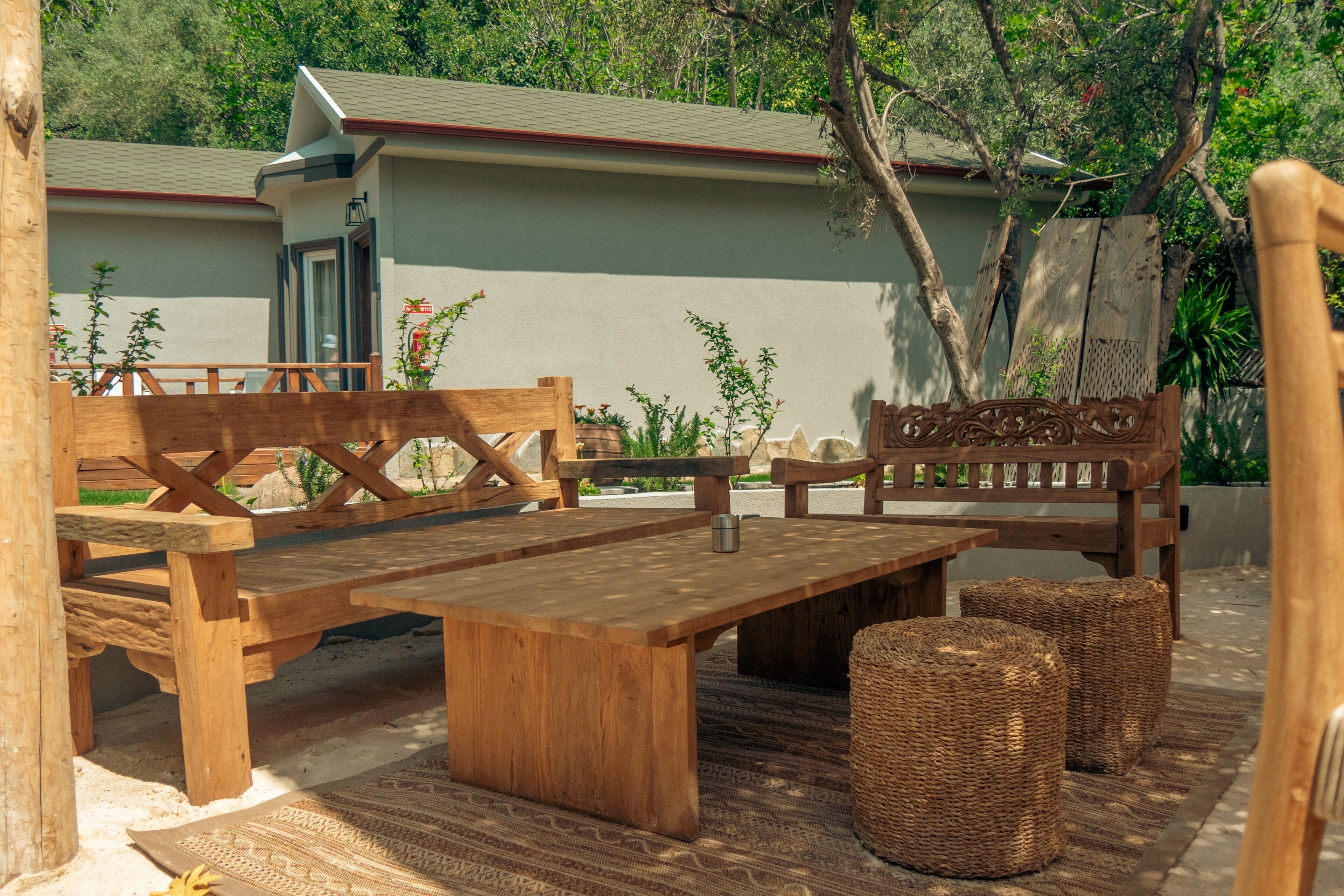 A wooden outdoor seating area with benches and a table, surrounded by wicker baskets and a patterned rug.