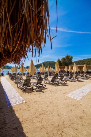 A beach with rows of sun loungers and umbrellas, a thatched roof structure, and a clear blue sky. - Beach 222 Ölüdeniz (Fethiye)