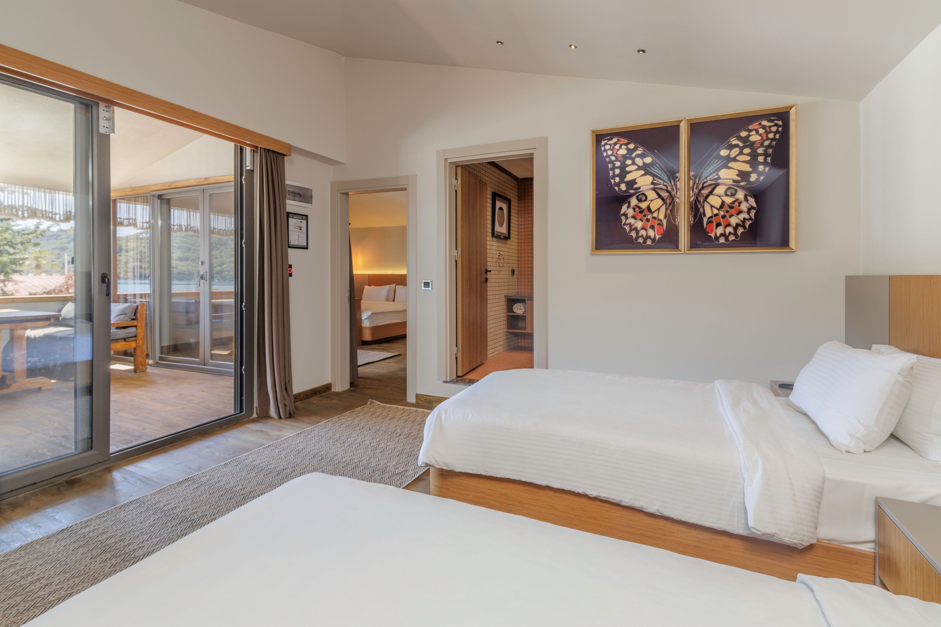 A bedroom with two beds, a sliding glass door to a balcony, and a framed butterfly artwork on the wall.