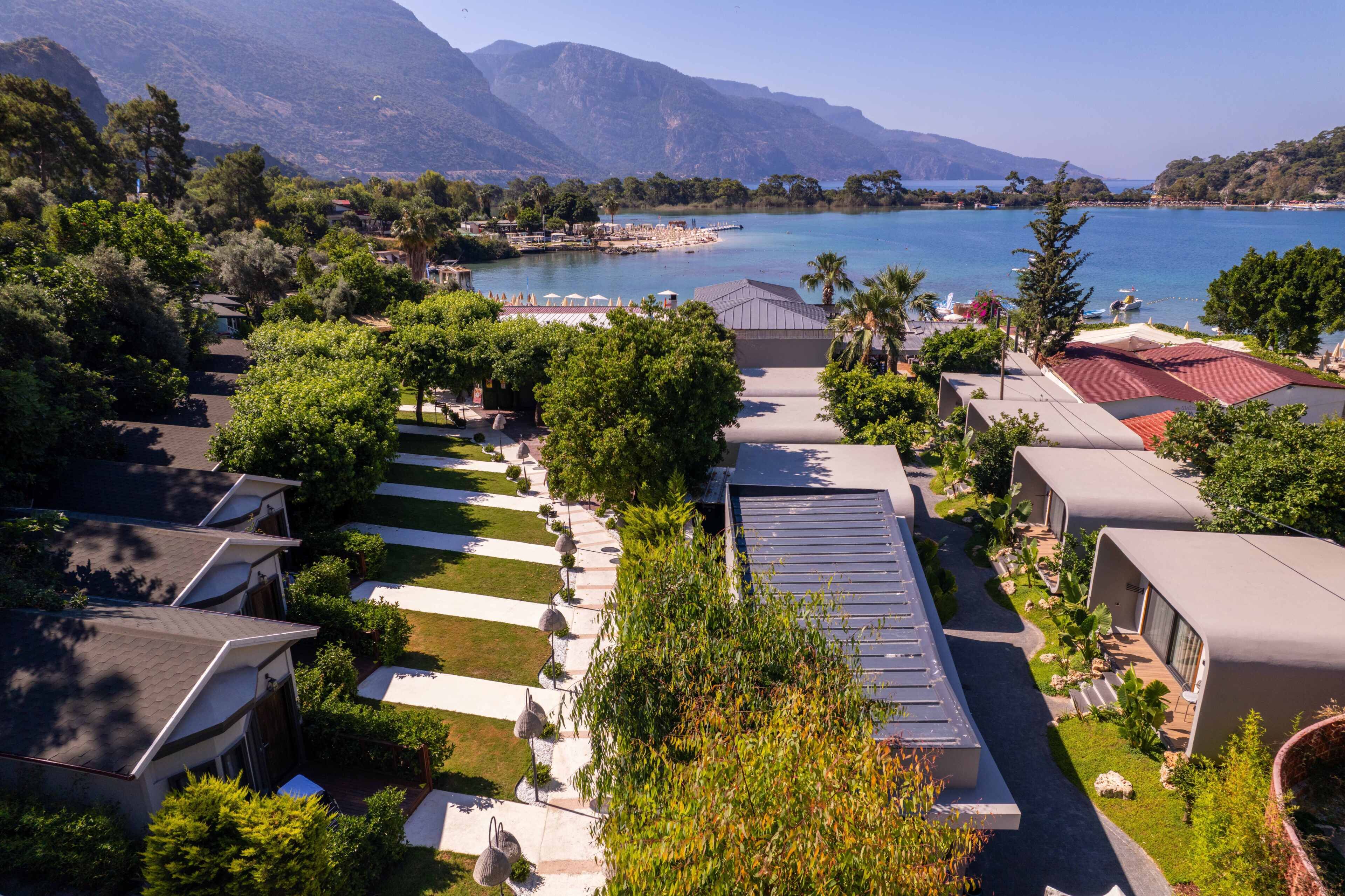 Un complex turístic amb diverses allotjaments de tipus bungalò, un camí central i vista al mar i a les muntanyes.