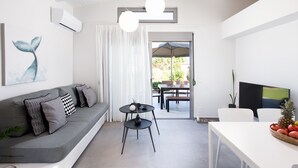 A modern living room with a grey sofa, a small round table, and a dining area with a white table and chairs.
