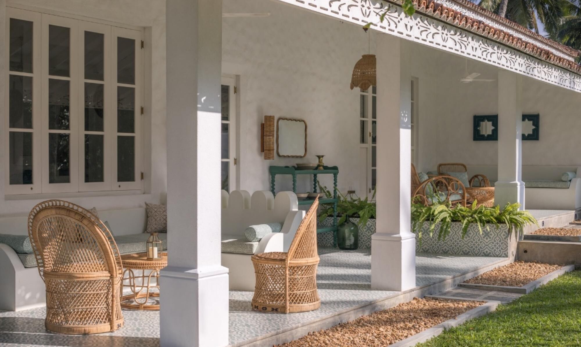Área externa coberta com móveis de vime, um pilar branco e uma pequena mesa com uma vela.