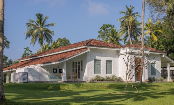 A white building with a red-tiled roof, surrounded by palm trees and a well-maintained lawn.