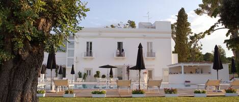 A white building with a swimming pool, outdoor seating, and umbrellas.