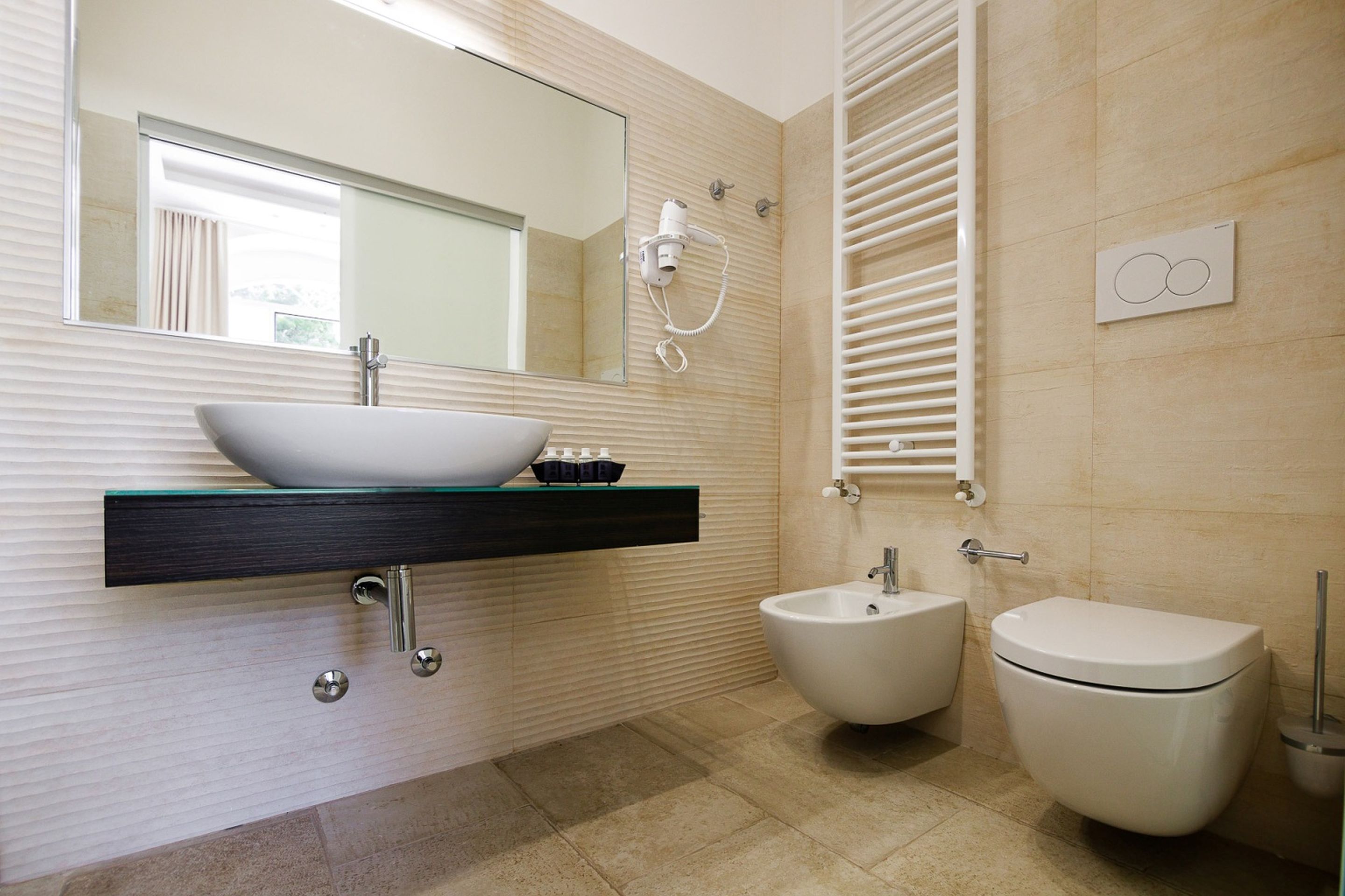 A modern bathroom with a vessel sink, bidet, and toilet.
