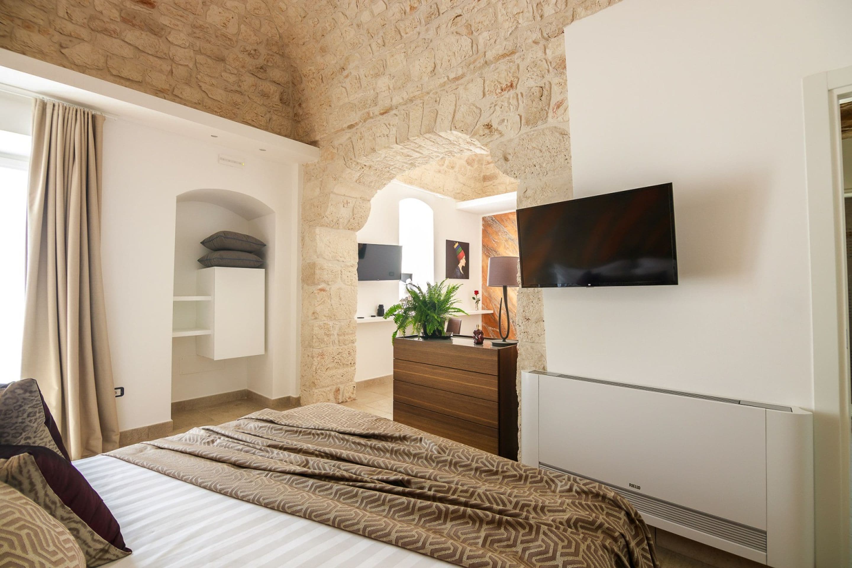 A bedroom with a bed, a dresser, a TV, and a stone wall.