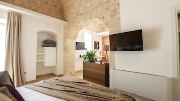 A bedroom with a bed, a dresser, a TV, and a stone wall.