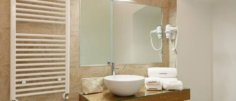 A modern bathroom with a glass sink, a towel rack, a mirror, and a towel warmer.