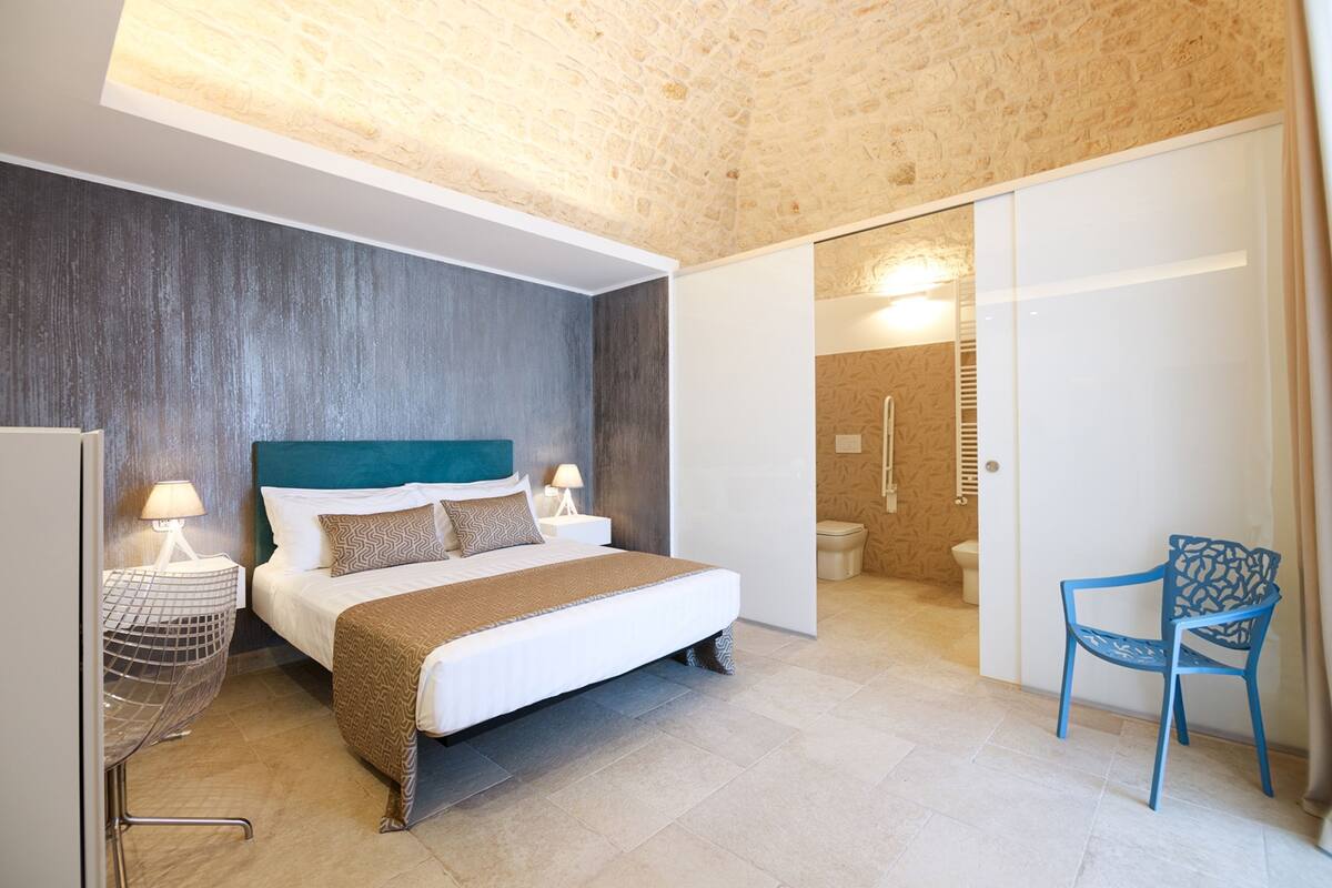A bedroom with a bed, bedside tables, a chair, and a bathroom with a shower.