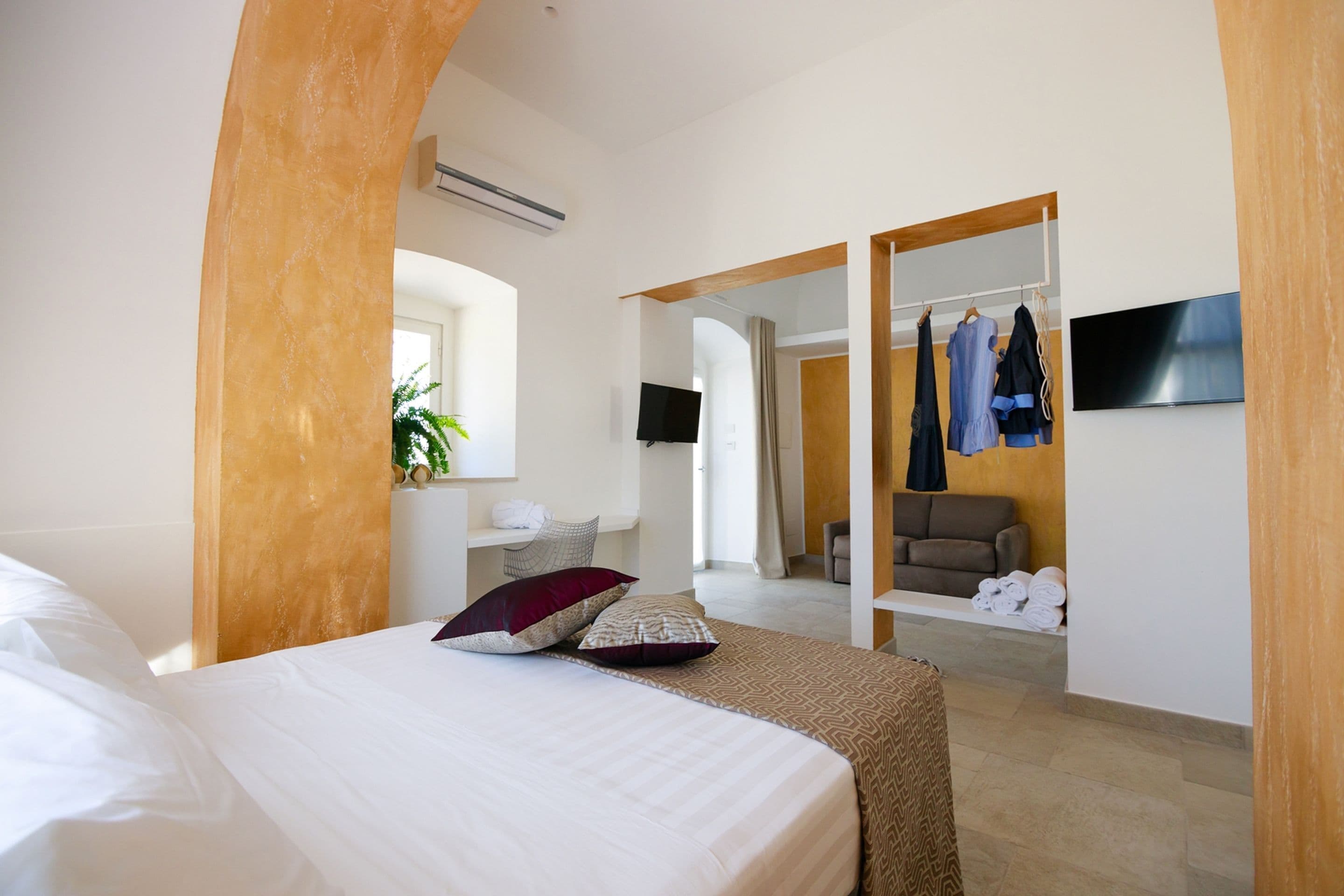 A hotel room with a bed, a TV, a mirror, and a clothing rack.