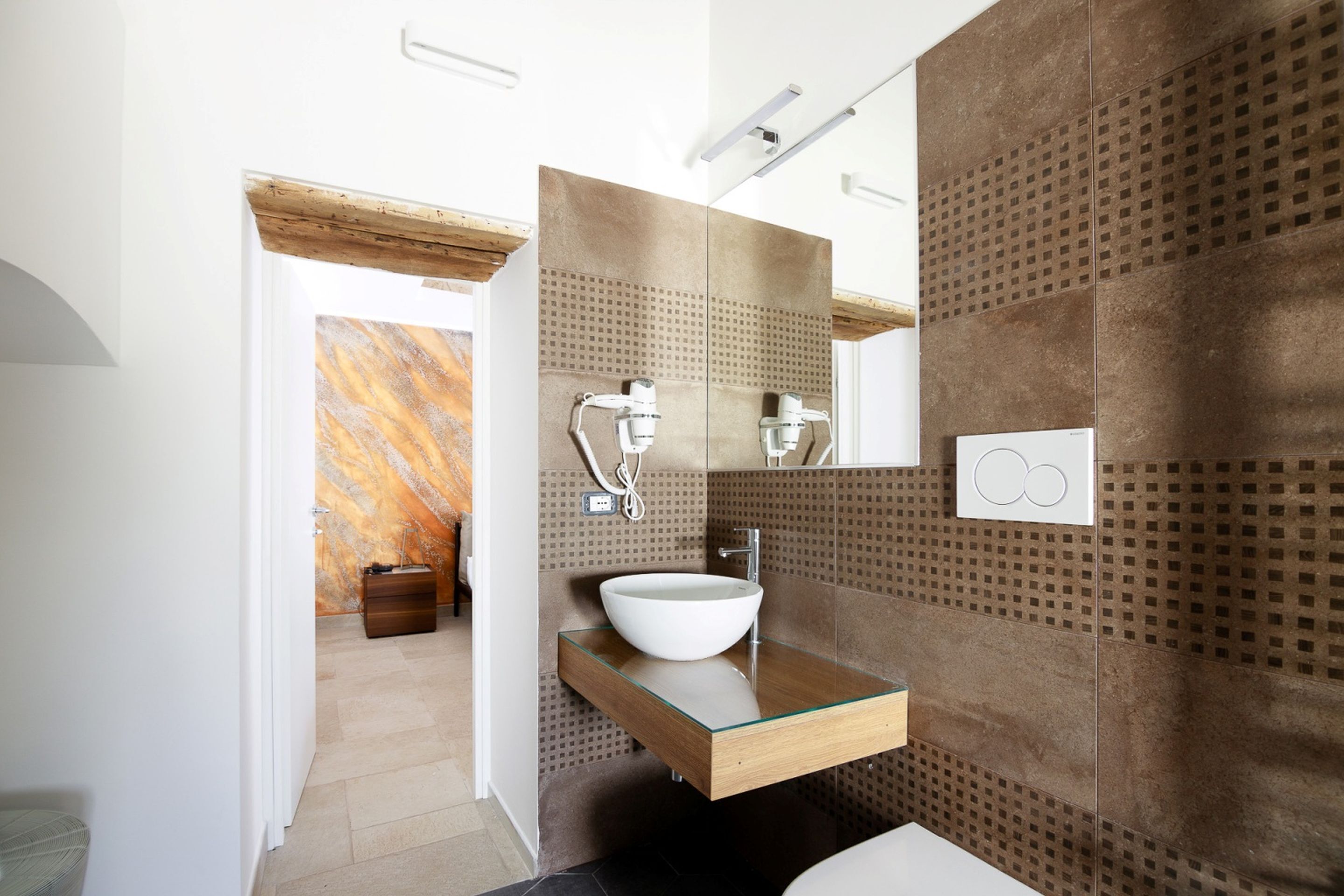 A modern bathroom with a glass sink, a large mirror, and a patterned wall.