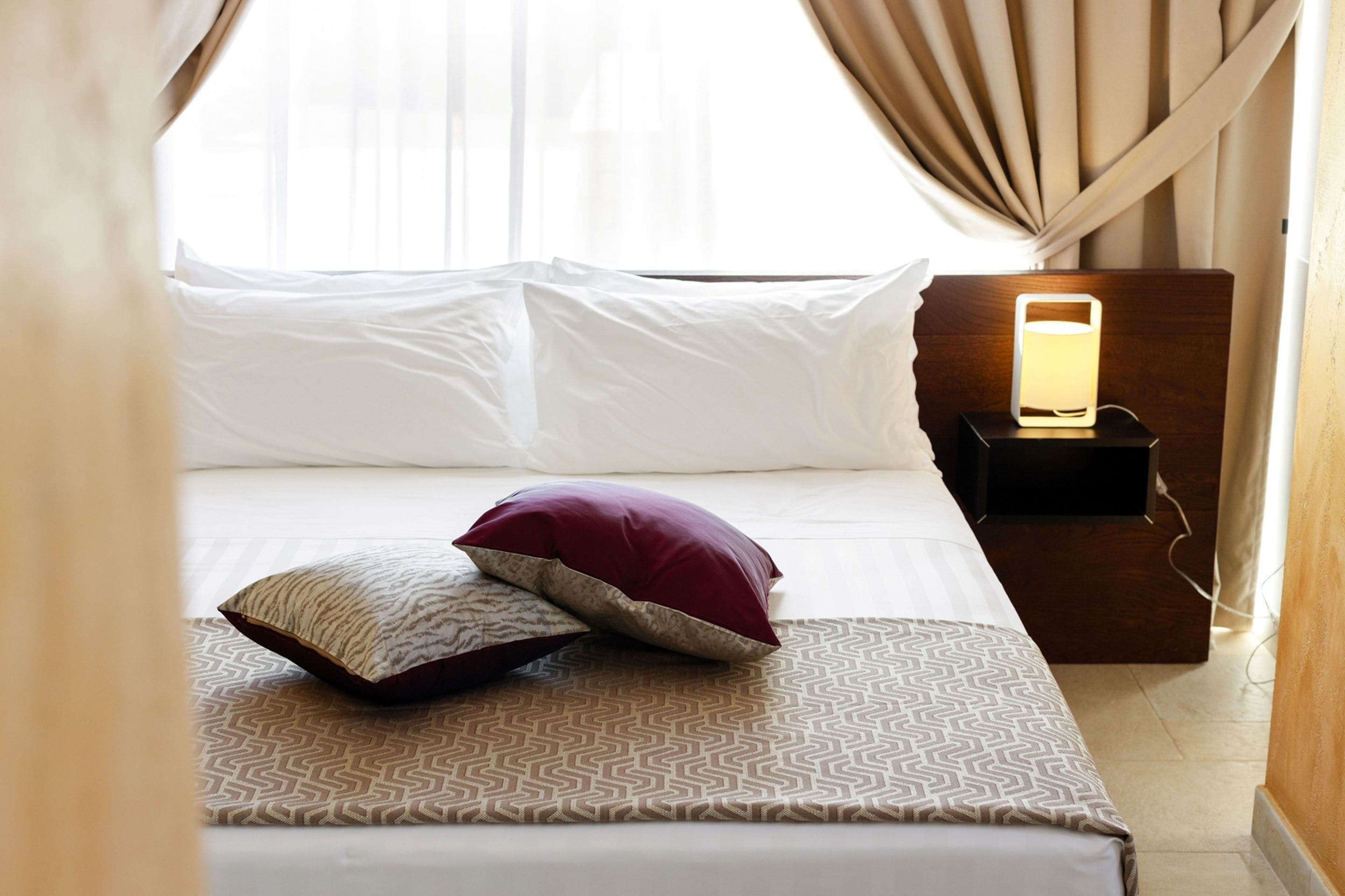 A neatly made bed with patterned bedding, a bedside lamp, and a window with curtains.