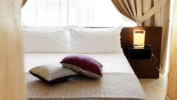 A neatly made bed with patterned bedding, a bedside lamp, and a window with curtains.