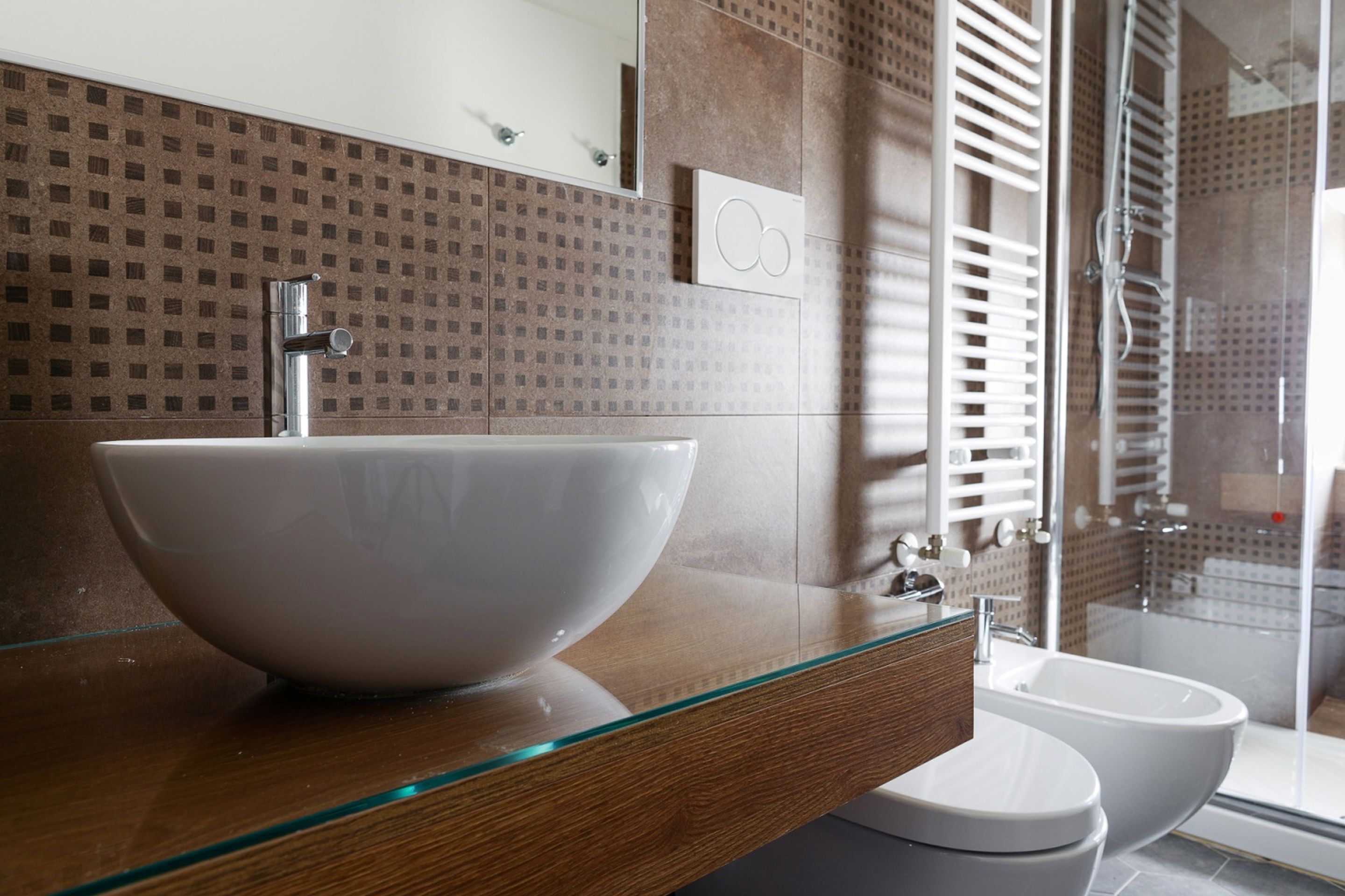 A modern bathroom with a large glass bowl sink, a wooden vanity, a glass shower enclosure, and a toilet.