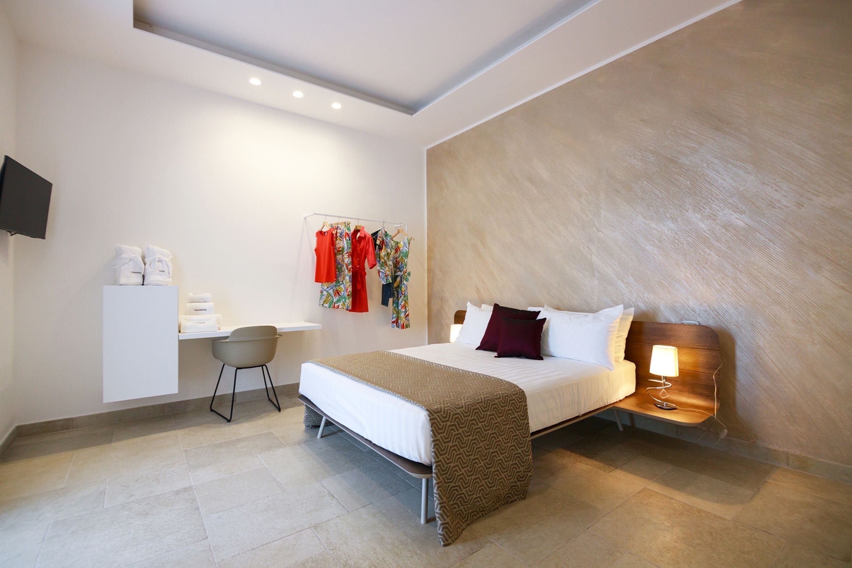 A modern hotel room with a bed, bedside table, and a desk with a chair.