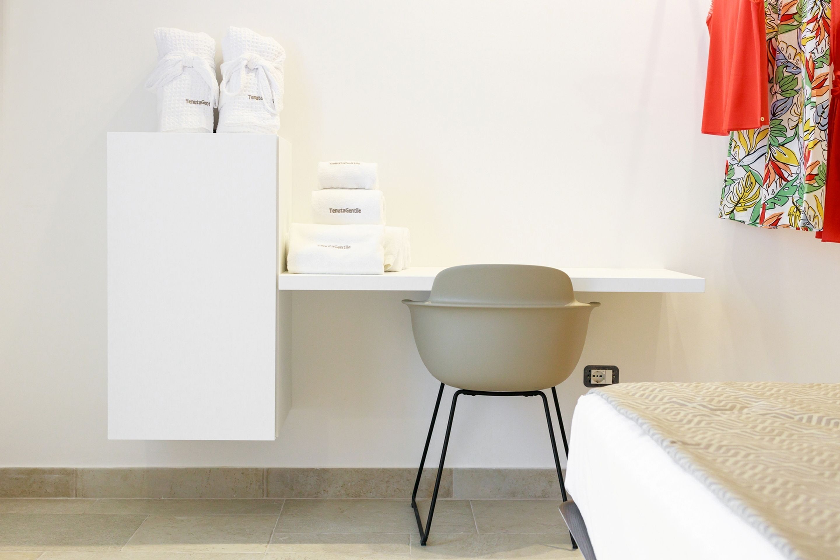 Ein Hotelzimmer mit Bett, Stuhl, Schreibtisch und Pflegeprodukten sowie einem farbenfrohen Vorhang.