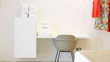 Ein Hotelzimmer mit Bett, Stuhl, Schreibtisch und Pflegeprodukten sowie einem farbenfrohen Vorhang.