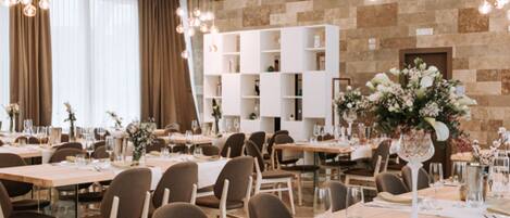 A modern dining area with wooden tables and chairs, a brick wall, and hanging light fixtures.