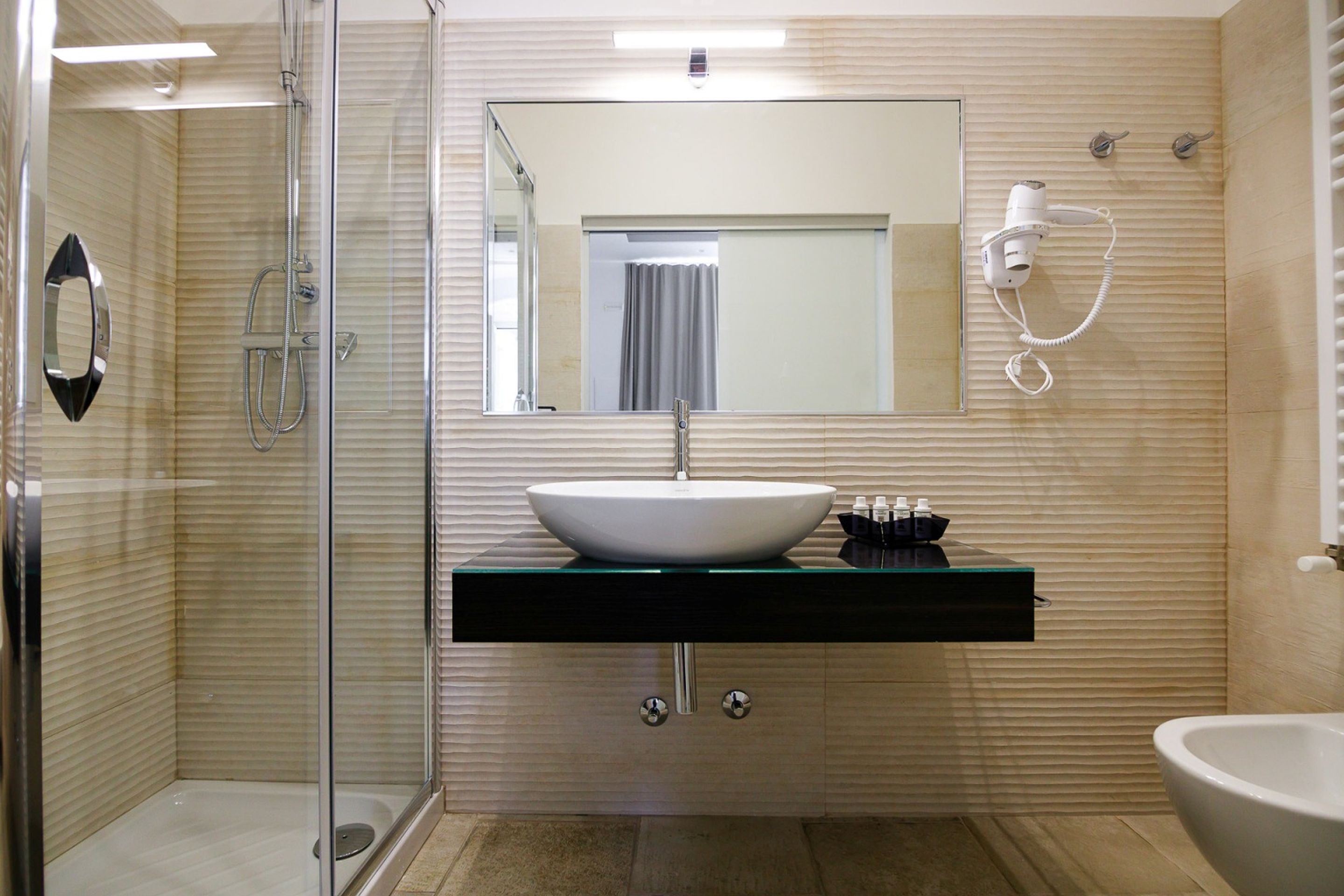 A modern bathroom with a glass-enclosed shower, a white sink with a black countertop, and a large mirror above the sink.