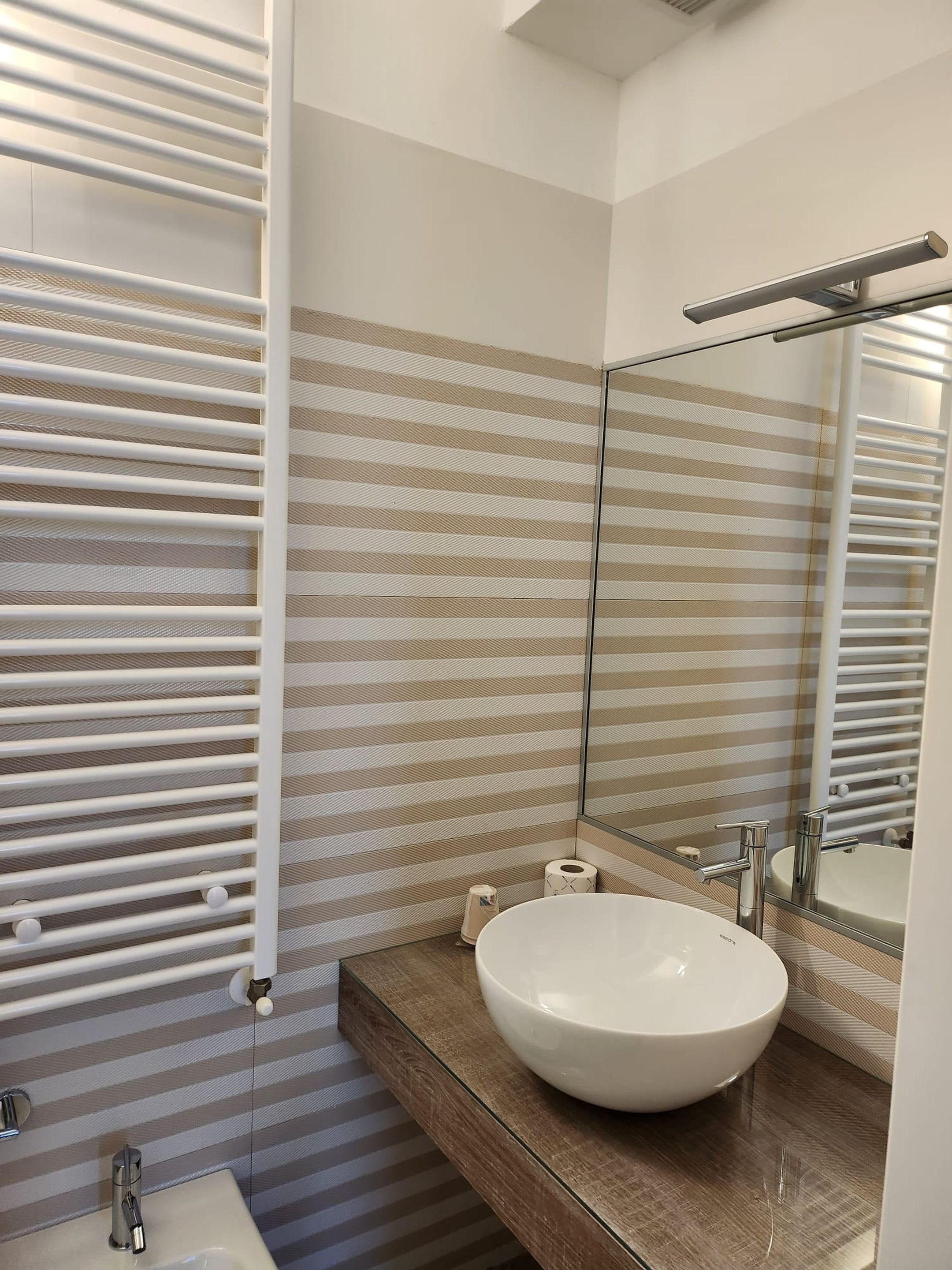 Un baño moderno con tocador de cubierta de vidrio, un espejo grande y un perchero para toallas.