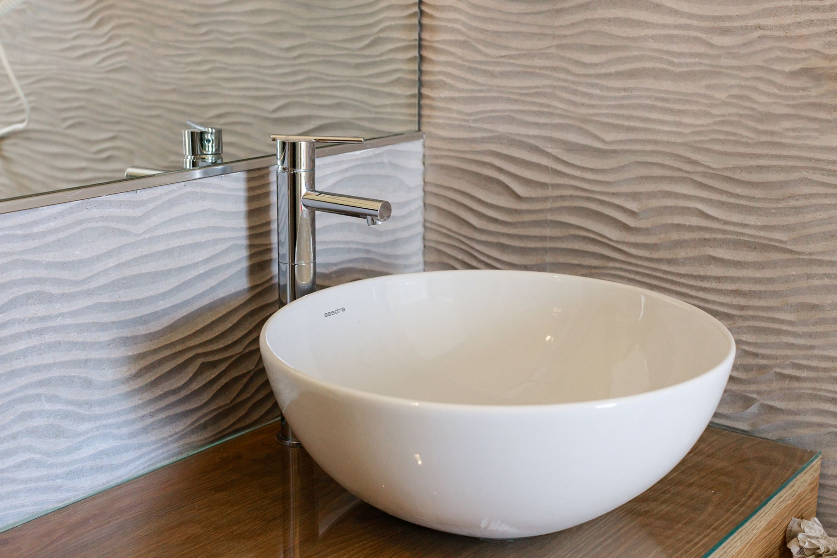 Une salle de bain moderne avec un lavabo en céramique blanche, un robinet chromé et un mur à texture.